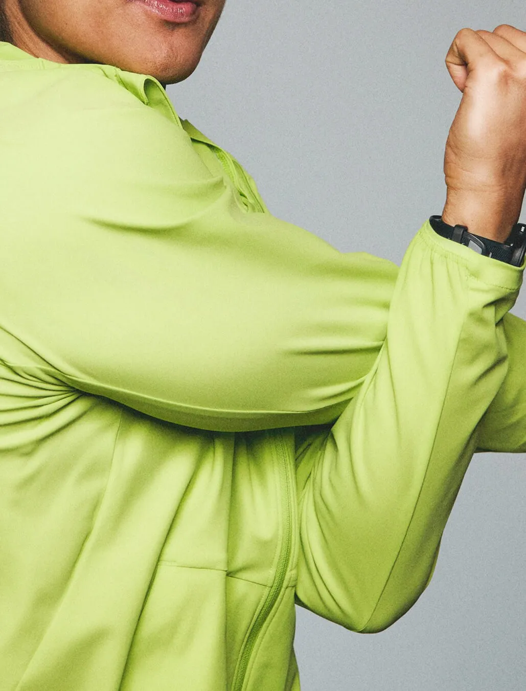 A person in a lime green long sleeve workout jacket doing a cross arm stretch